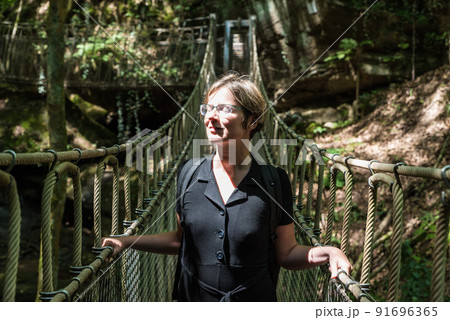 Portrait of a woman at a wooden suspension bridge over a small creek valley in the woods Portrait of a woman at a wooden suspension bridge over a small creek valley in the woods 91696365