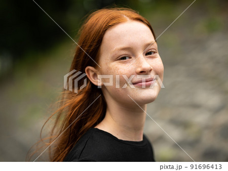 Red haired twelve year old girl with freckles posing with a nature bokeh background 91696413