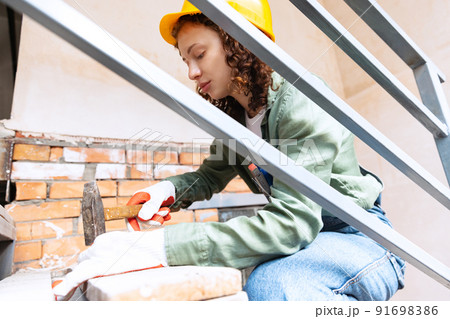 Live portrait of young woman, builder wearing helmet using different work tools at a construction site. Gender equality, job, work concept 91698386