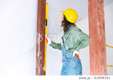 Live portrait of young woman, builder wearing helmet using different work tools at a construction site. Gender equality, job, work concept Live portrait of young woman, builder wearing helmet using different work tools at a construction site. Gender equality, job, work concept 91698391