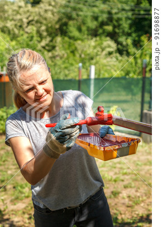 Young woman paints red primer metal structure Young woman paints red primer metal structure 91698877