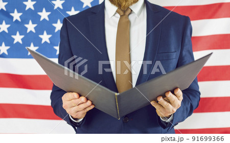 Close up of open folder in hands of unknown man in business suit on background of American flag. 91699366