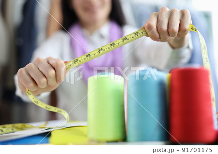 Seamstress holds tape measure in sewing workshop Seamstress holds tape measure in sewing workshop 91701175