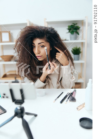 Talented tanned handsome curly Latin beauty blogger in linen shirt do smoky eyes for diy in home white interior. Copy space Mockup Banner. Influencer record video review blog using smartphone Talented tanned handsome curly Latin beauty blogger in linen shirt do smoky eyes for diy in home white interior. Copy space Mockup Banner. Influencer record video review blog using smartphone 91702110