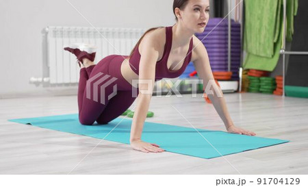 a beautiful and slender woman in a burgundy tracksuit exercises on a mat 91704129