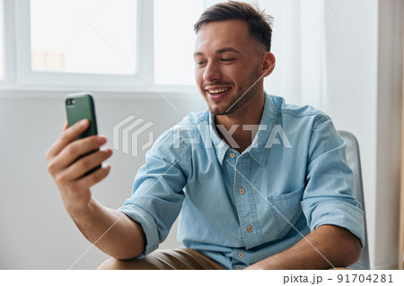 Smiling cute happy talking about his business to audience attractive young man looks at screen hold phone record video review at home. New profession Online influencer blogger concept Smiling cute happy talking about his business to audience attractive young man looks at screen hold phone record video review at home. New profession Online influencer blogger concept 91704281