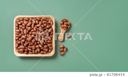 Raw organic peanut on a square wooden plate over green background. 91706454