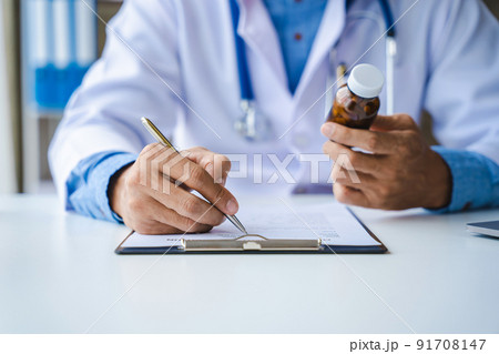 Close-up of doctor's hands writing prescription and holding bottle with pills. Healthcare, medical and pharmacy concept. 91708147