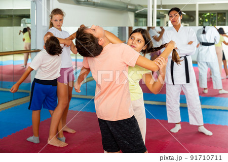 kids in pair exercising self-defense movements during group class with female coach 91710711
