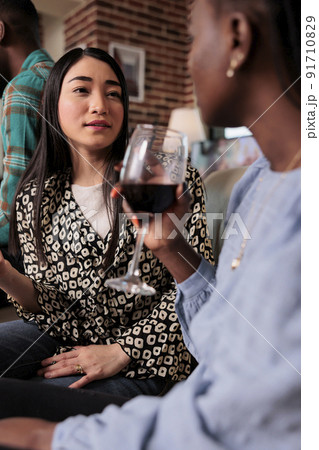 Multiethnic happy people celebrating birthday event while drinking alcoholic beverages. Cheerful smiling diverse women sitting on sofa at wine party while enjoying fun time together. Multiethnic happy people celebrating birthday event while drinking alcoholic beverages. Cheerful smiling diverse women sitting on sofa at wine party while enjoying fun time together. 91710829