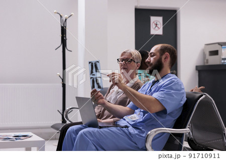 Medical assistant showing x ray to elderly patient, sitting in hospital reception lobby. Nurse explaining radiography scan results to woman with disease, talking about treatment and diagnosis. 91710911