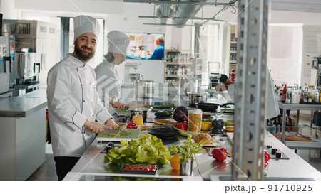 Portrait of man in uniform preparing green salad on cutting board to cook gastronomy cuisine dish for restaurant menu. Professional chef working on culinary recipe with organic food. Handheld shot. 91710925