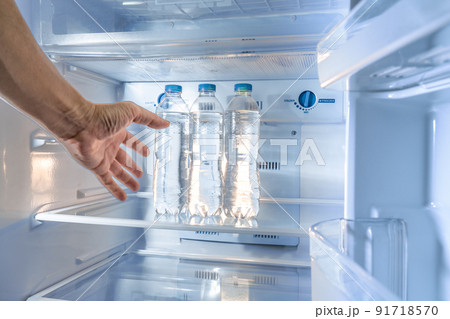 A shaky thirsty male's hand reaching out to grab a cold water bottle from a refrigerator, motion added to the hand A shaky thirsty male's hand reaching out to grab a cold water bottle from a refrigerator, motion added to the hand 91718570
