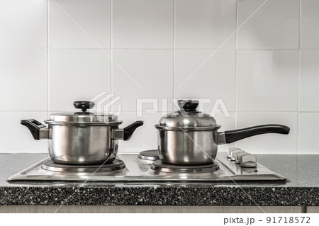 Couple of stainless pots on kitchen stove with marble counter top and white tile wall Couple of stainless pots on kitchen stove with marble counter top and white tile wall 91718572