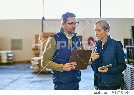 These shipments are a priority. Shot of two people looking at paperwork while working in a warehouse. These shipments are a priority. Shot of two people looking at paperwork while working in a warehouse. 91719640