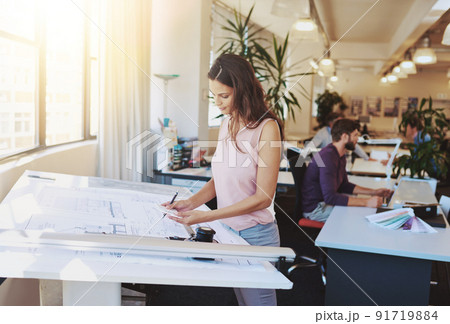 Working on a new building plan. Cropped shot of a young architect working on her drafting table. 91719884