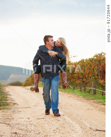Having fun while messing around. A young man carrying his girlfriend on his back while taking a walk on a vineyard. 91720644