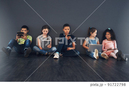 Growing up in the digital age. Studio shot of kids sitting on the floor and using wireless technology against a gray background. 91722798