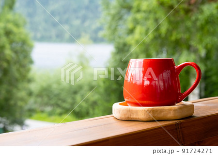 Morning coffee in garden. Red mug on wooden board against blurred nature. Morning coffee in garden. Red mug on wooden board against blurred nature. 91724271