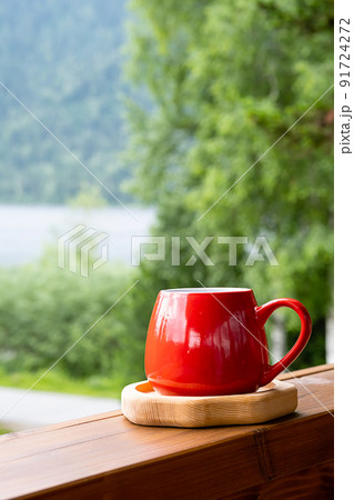 Morning coffee in garden. Red mug on wooden board against blurred nature. 91724272