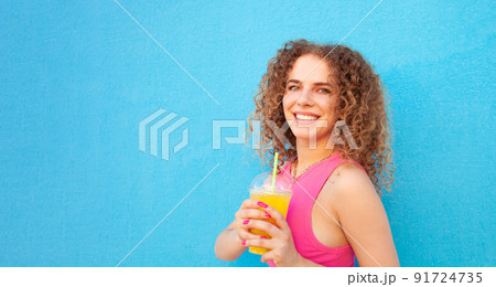 beautiful woman holds delicious orange juice, cold refreshing summer drink. Blue background, isolated. Outdoors, walk around city. Happy 91724735