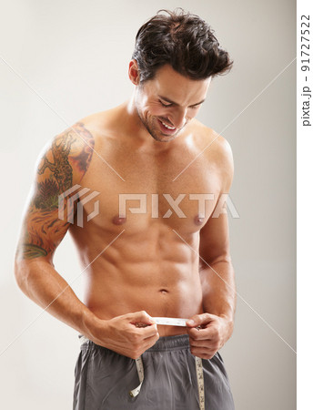 Proud of his rock hard abs. A hunky young man measuring his stomach. 91727522