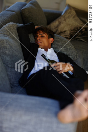 Sleeping off that hangover. Shot of a young man lying passed out on a sofa while holding a bottle of wine. 91728484