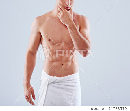 Abs-alicious. Cropped studio shot of a handsome bare chested young man with his waist wrapped in a towel. Abs-alicious. Cropped studio shot of a handsome bare chested young man with his waist wrapped in a towel. 91728550