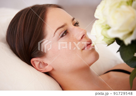 Her heart is won. A beautiful young woman lying down and admiring the bouquet of white roses she is holding. 91729548
