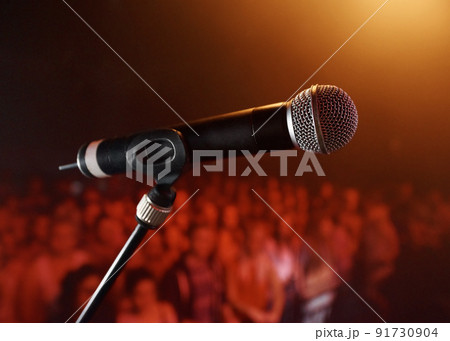 Take the stage.... A microphone standing on a stage with a crowd in the background. 91730904