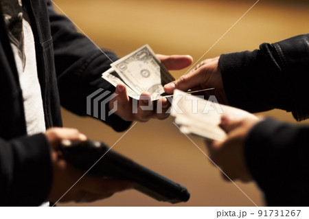 Sealing the deal. Hands holding cash and a gun passing money between them. Sealing the deal. Hands holding cash and a gun passing money between them. 91731267