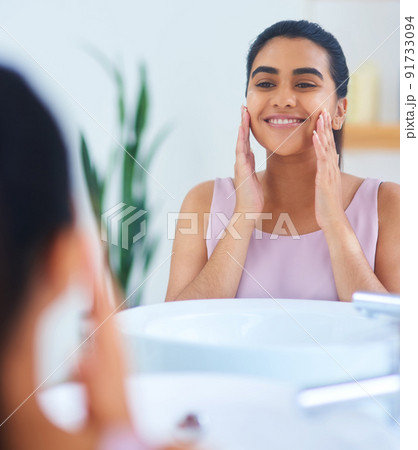 Not a single blemish in sight. Shot of a young woman applying moisturiser to her face in a bathroom at home. Not a single blemish in sight. Shot of a young woman applying moisturiser to her face in a bathroom at home. 91733094