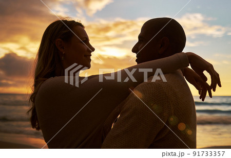 Loving young affectionate interracial couple in silhouette facing each other while spending time together on the beach at sunset. Lovers sharing romantic moment against golden sky while on vacation Loving young affectionate interracial couple in silhouette facing each other while spending time together on the beach at sunset. Lovers sharing romantic moment against golden sky while on vacation 91733357
