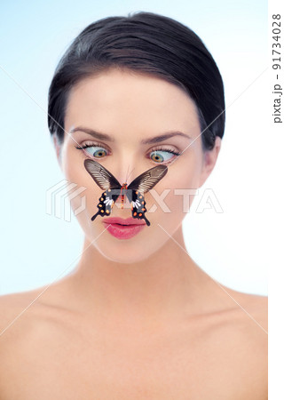 Soft and natural skincare. A woman looking down cross-eyed at a butterfly on her nose. 91734028
