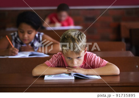 School sucks. A young boy resting his head on his arms as he sits in a classroom looking bored. School sucks. A young boy resting his head on his arms as he sits in a classroom looking bored. 91735895