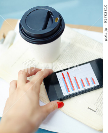 Working outside the office. Hand holding smartphone with bar chart on screen with disposable cup, pen, newspaper and clipboard. 91738810