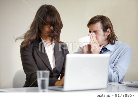 Showing poor manners. A young businessman blowing his nose all over a coworker. 91738957