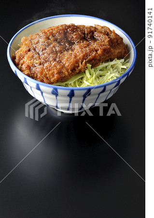 繊切りキャベツの上にたっぷりのソースが絡んだカツが乗っている熱々のソースかつ丼を黒背景で撮影 91740141
