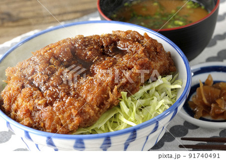繊切りキャベツの上にたっぷりのソースが絡んだカツが乗っている熱々ソースかつ丼と味噌汁と漬物 91740491