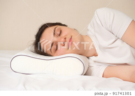 A woman sleeps on an orthopedic pillow made of memory foam, lying on a bed. The correct pillow for a comfortable healthy sleep. 91741301