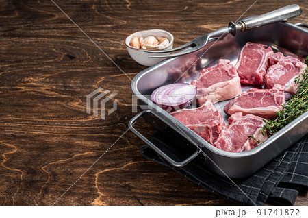 Uncooked Raw lamb loin chops steaks, saddle in kitchen tray with herbs. Wooden background. Top view. Copy space 91741872