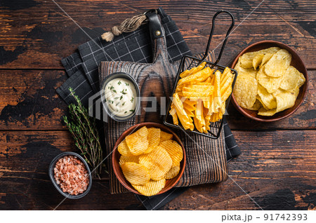 Mix of Crinkle Potato chips served with dip sauce and sea salt. Wooden background. Top view 91742393