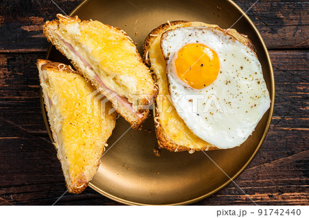 French toasts Croque monsieur and croque madame, grilled sandwiches on brioch bread with sliced ham, melted emmental cheese and egg. Wooden background. Top view French toasts Croque monsieur and croque madame, grilled sandwiches on brioch bread with sliced ham, melted emmental cheese and egg. Wooden background. Top view 91742440