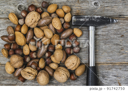 Hammer and pile of various nuts on a wooden background 91742750