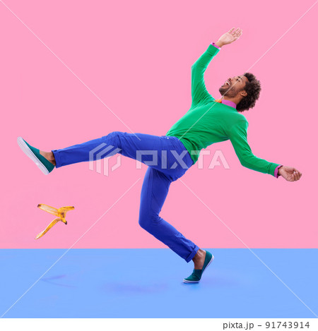Watch your step.... Humorous shot of a young man slipping on a banana peel agains a colorful studio background. 91743914