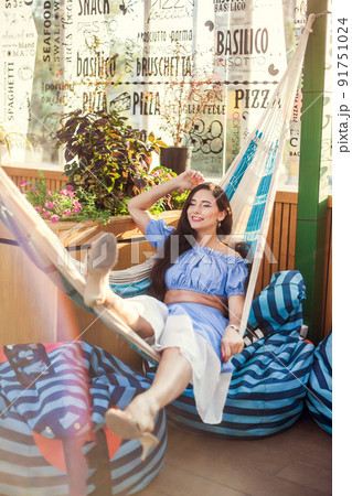 A beautiful young woman lies in a hammock on the summer terrace of a city cafe and enjoys the summer 91751024