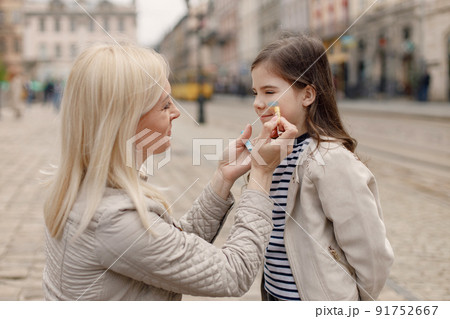 Young mother drawing on a cheek of her daughter with pencils. Blonde woman drawing blue and yellow colours. Woman and girl supporting Ukraine against war. 91752667