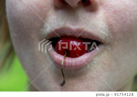 Composition of a sweet cherry and a natural hairy upper lip of a body positive young woman. Composition of a sweet cherry and a natural hairy upper lip of a body positive young woman. 91754128