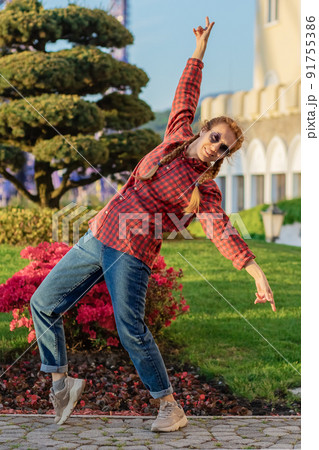 A girl in a youth shirt and jeans in a pose of bending over and spreading her arms against the background of a flower bed with a tropical tree and flowers A girl in a youth shirt and jeans in a pose of bending over and spreading her arms against the background of a flower bed with a tropical tree and flowers 91755386