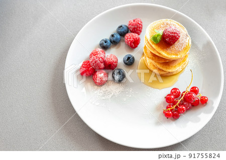 Pancakes on a white plate on a light background with berries and honey. empty space for text. 91755824